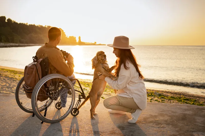 Un homme en fauteuil roulant au bord de la mer avec une proche et son chien
